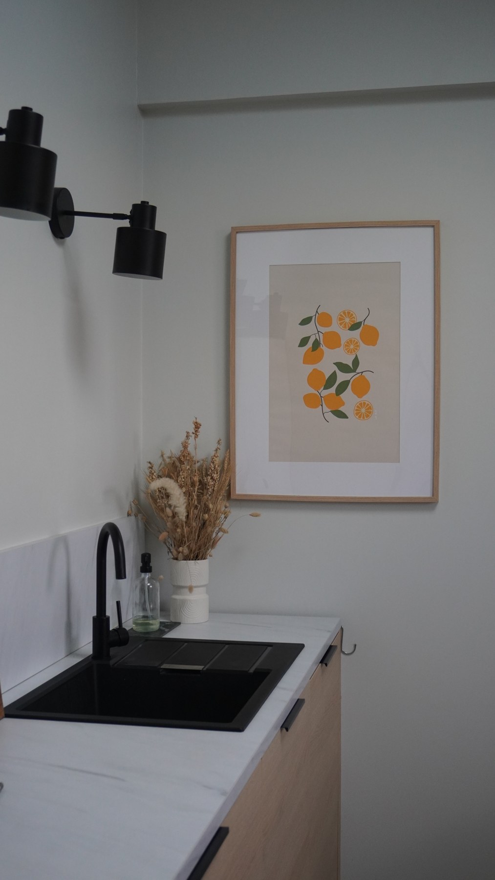 Cuisine vitaminée : évier noir, façades en bois et affiche d’agrumes